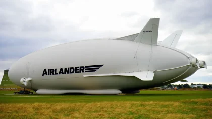 Un dirigible surcando nubes de tormenta sobre un vasto paisaje fantástico con criaturas colosales en el horizonte
