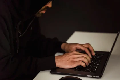 Figura anónima frente a pantalla iluminada en la oscuridad, simbolizando actividad cibernética y filtración de datos