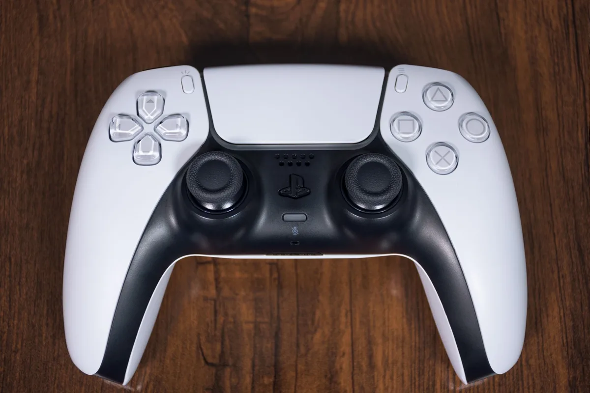 Manos sosteniendo un controlador de videojuegos frente a una pantalla con perspectiva de cámara alejada