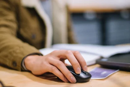 Mano ajustando la rueda de un ratón moderno sobre un escritorio con monitor de alta resolución de fondo
