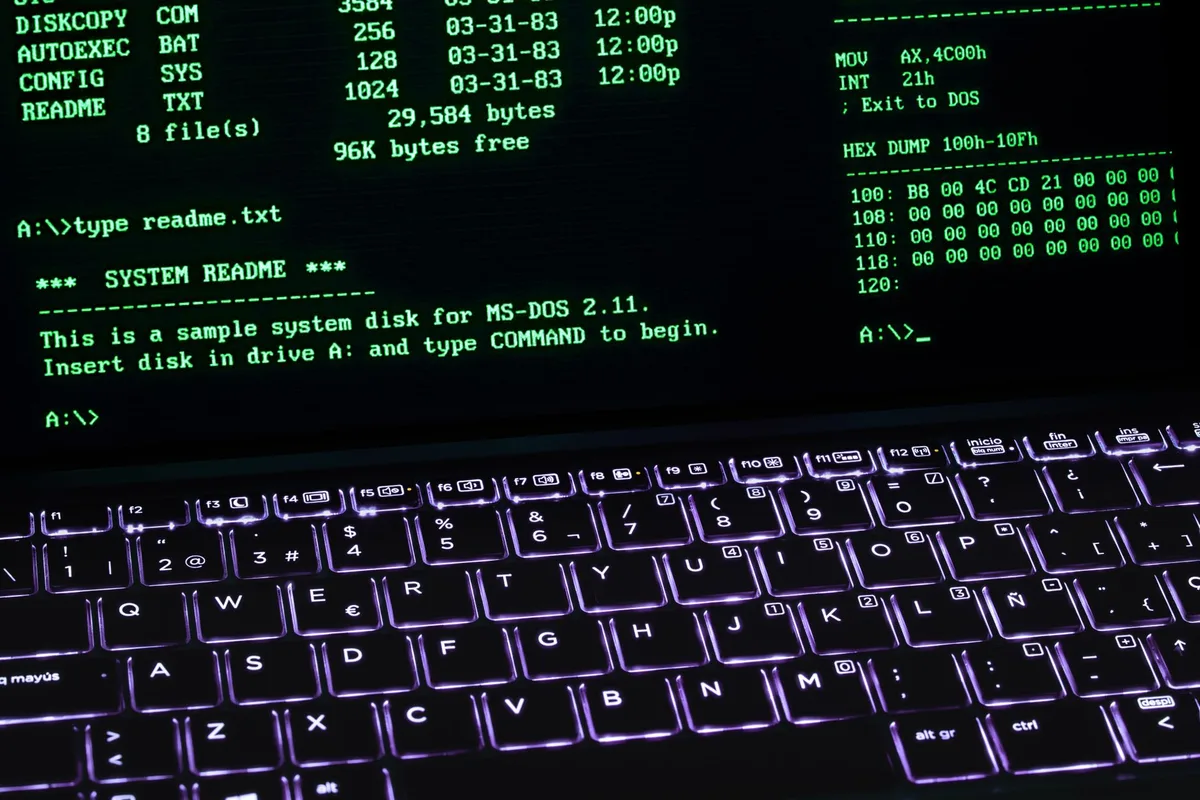 Mano escribiendo código en terminal Linux con interfaz Windows visible en el monitor de un desarrollador