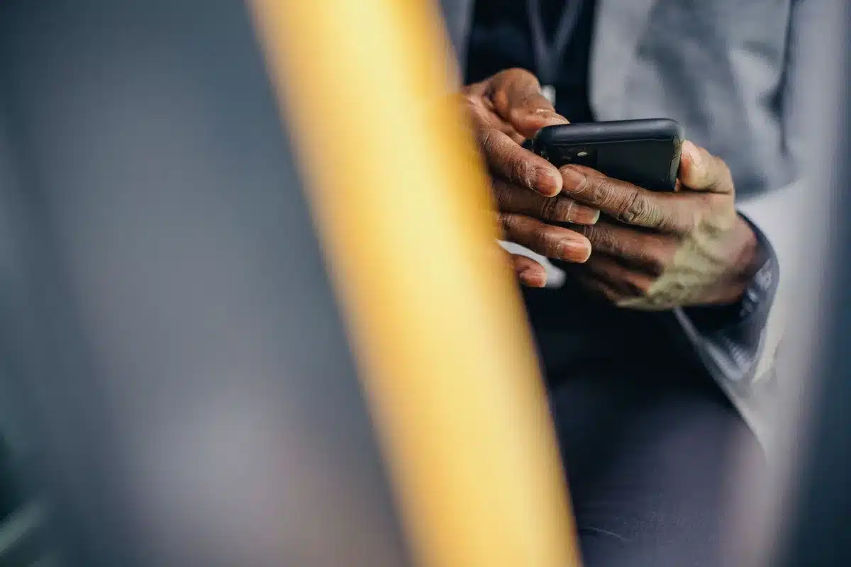 Anonymous hands holding a generic smartphone showing a bright AMOLED screen, no brand visible, crowded café background blurred