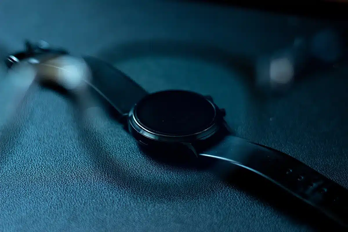 An anonymous runner glancing at an unbranded smartwatch display showing a readiness score on screen, blurred track in background