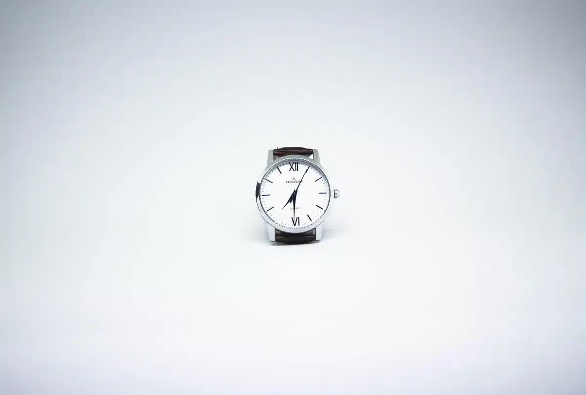 An anonymous close-up of an unbranded running watch face displaying time and simple icons on its screen, set on a neutral wooden table with a pair of running shoes blurred in background