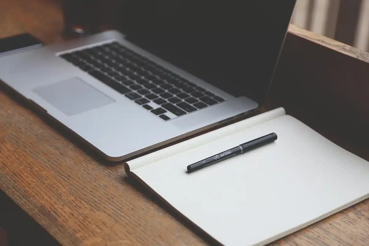 a minimal desktop workspace with a laptop showing a blank chat window, a notepad with handwritten prompts, and a mug beside it