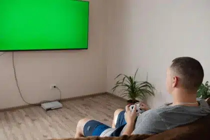 Manos sujetando un mando frente a una televisión con menú de juegos desenfocado