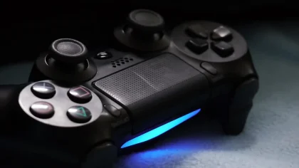 Mano sujetando un mando de PlayStation frente a una pantalla con iconos de recompensas digitales