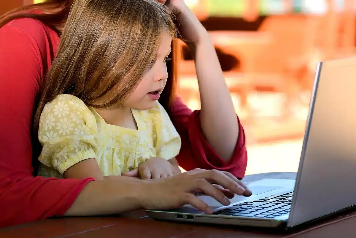 Manos de adulto y niño usando un ordenador y una tableta, representando control parental