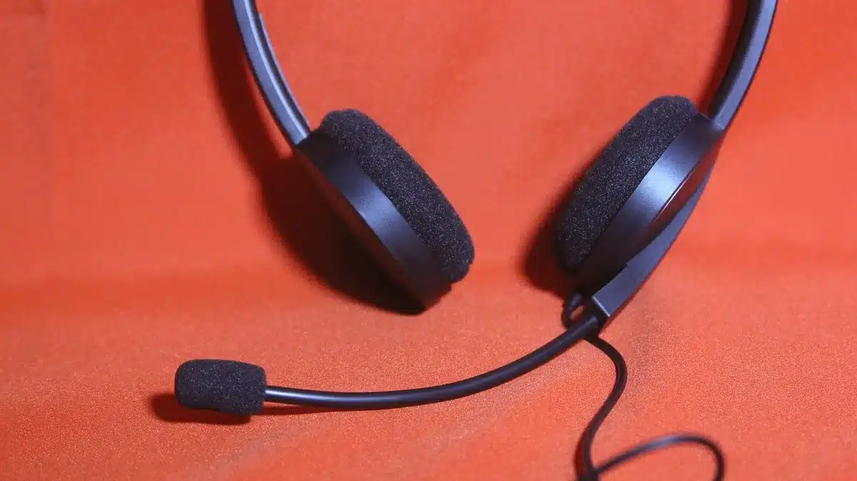 Empty office with a single anonymous headset on the desk, a Windows laptop screen dimmed in the background