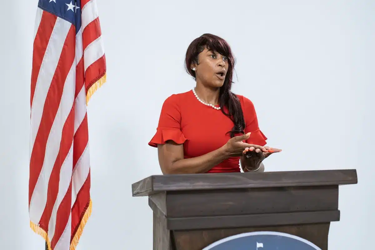 empty podium under a single spotlight with a lone microphone on a stand, dust motes visible, a folded sheet of paper on the floor, sense of caution