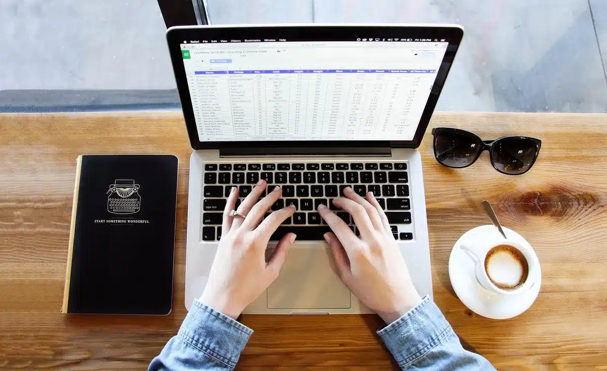 Escritorio con portátil cerrado, cuaderno y unidad de disco externa, manos anónimas sobre teclado