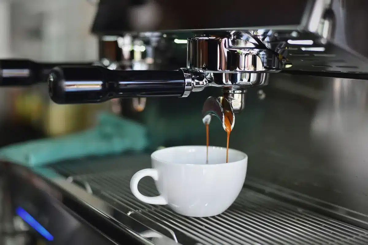 A clean kitchen countertop with an unbranded black automatic coffee machine, a closed bean hopper, and a small cup of espresso beside it