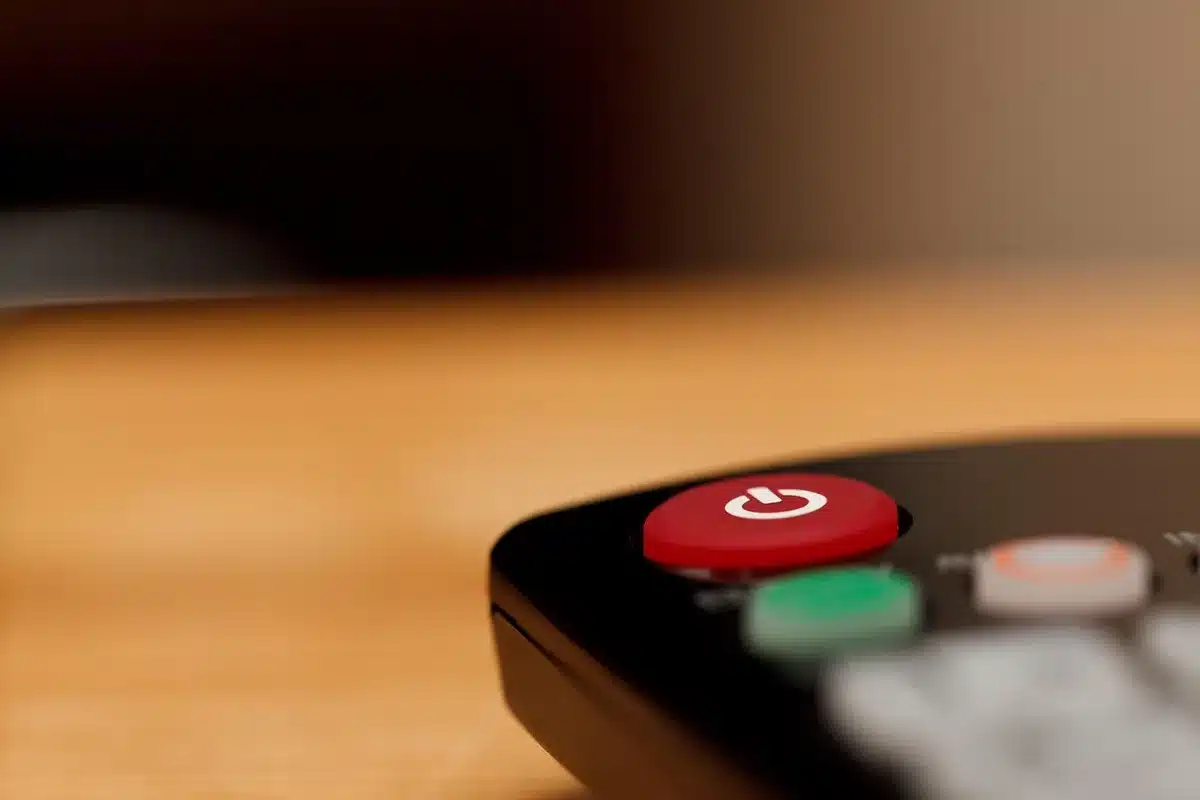 Close shot of a sleek unbranded TV remote on a coffee table, blurred screen in background, anonymous home setting