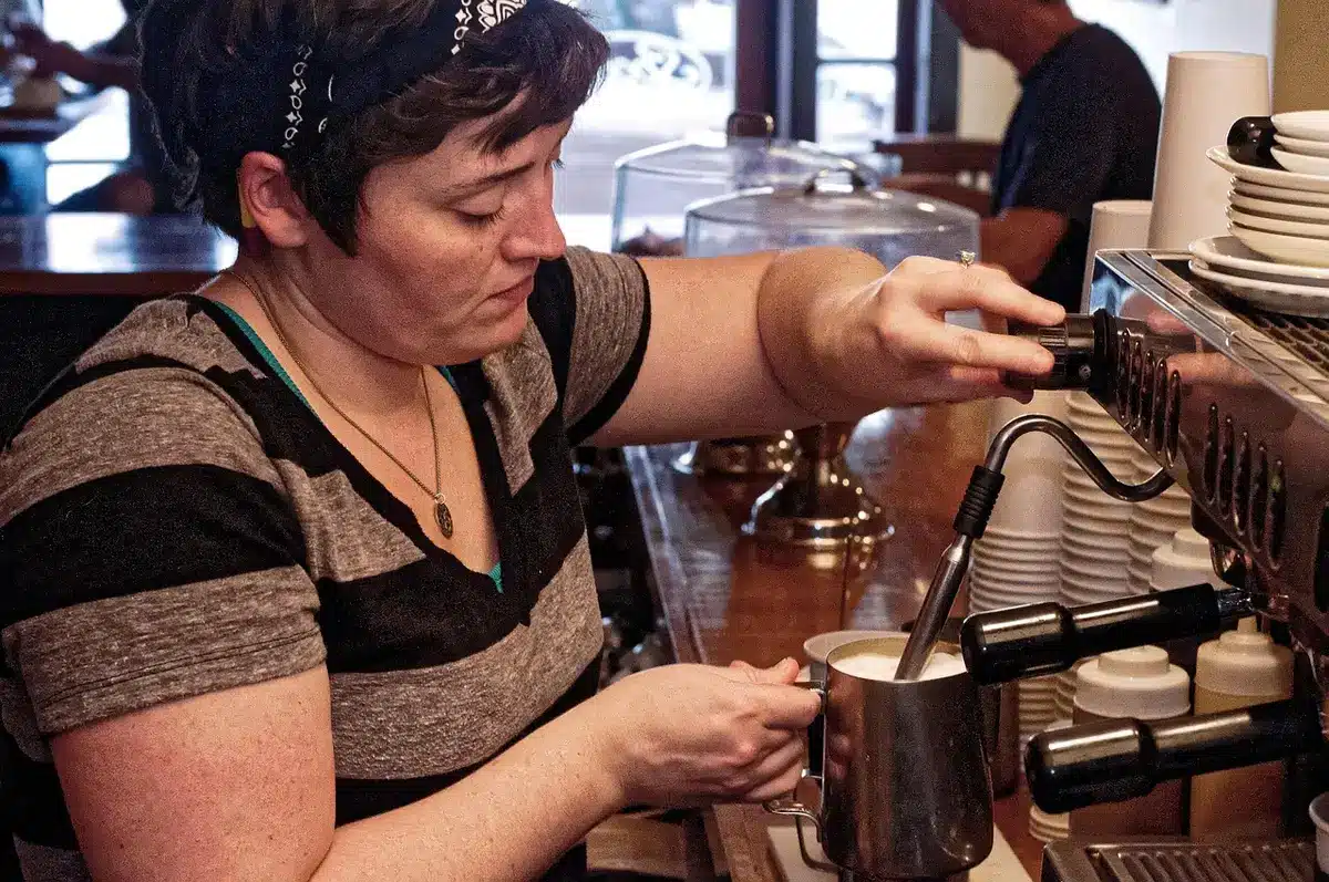 Scene of a compact espresso machine on a kitchen counter, small milk jug beside it, steam rising from the spout, no brand visible