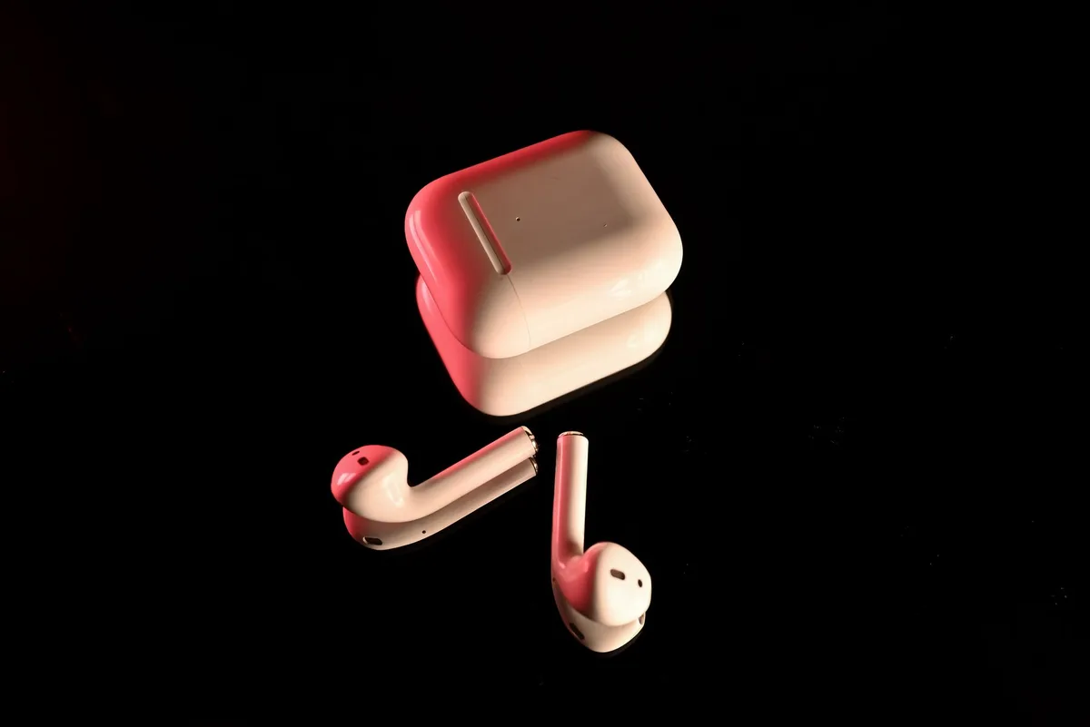 A close-up of two compact wireless earbuds resting beside an open charging case on a neutral surface, no logos or text