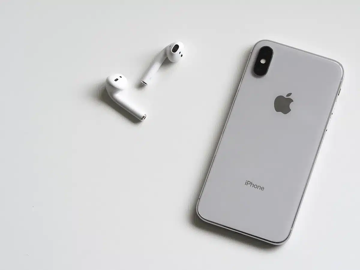 Empty studio table with a compact unbranded smartphone mockup and a detached camera lens nearby, soft daylight, neutral background