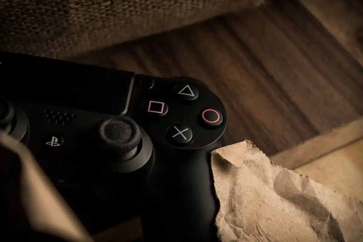 Close-up of a DualSense controller resting on a table beside a TV remote and an open PS5 media menu on the screen, anonymous and unbranded