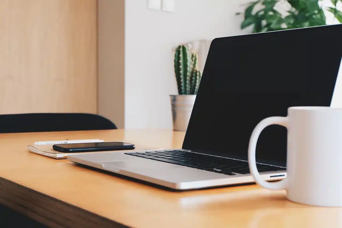 Silver MacBook-like laptop on a clean wooden desk with anonymous hands reaching, open to a coding editor screen