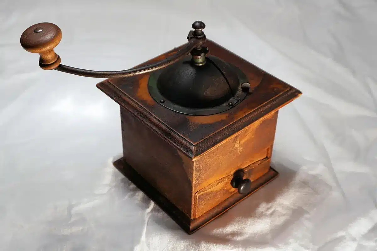 Close-up of a coffee grinder, scattered roasted beans and a tamping tool on a wooden surface, shallow depth of field