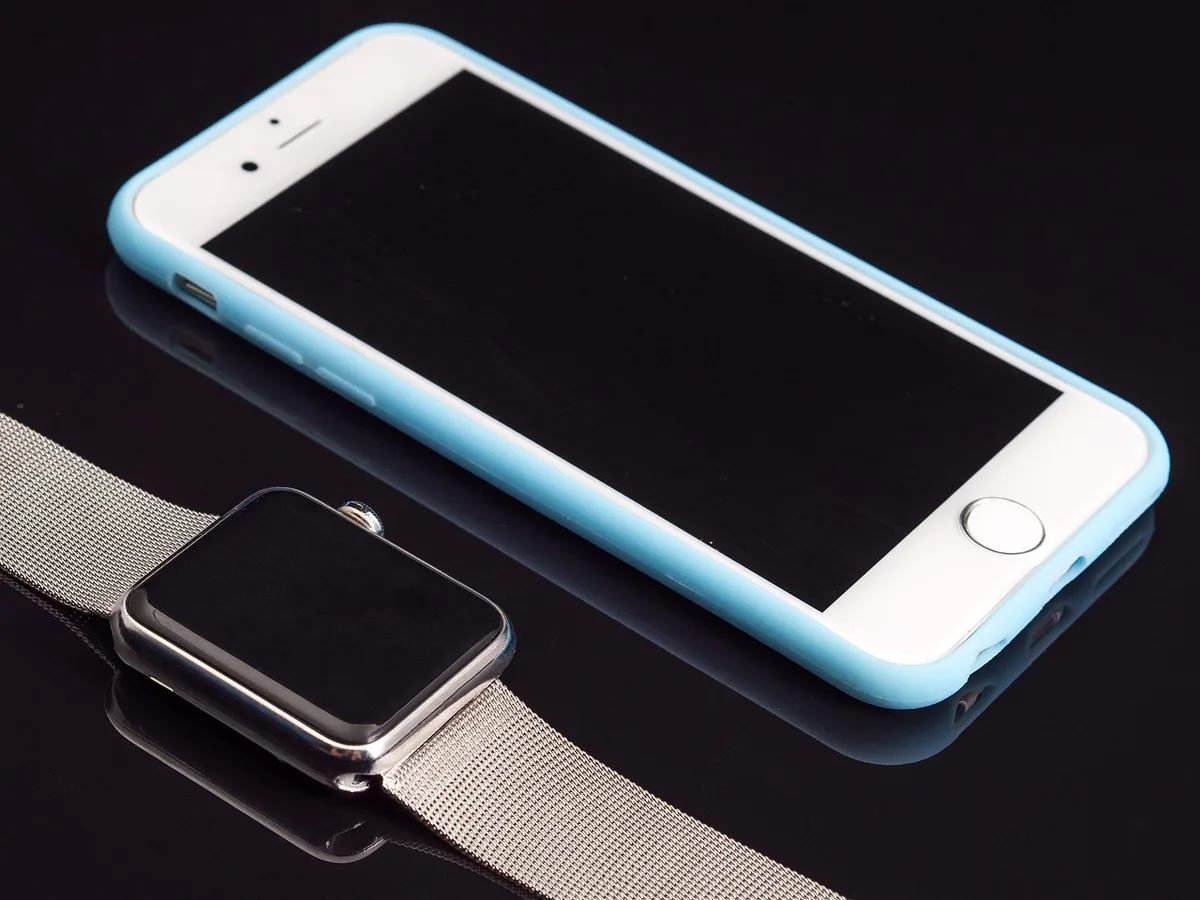 A compact retail bundle on a neutral table: an unbranded modern smartphone next to an anonymous slim fitness watch, both slightly angled, a small price tag card reading no text, soft studio light
