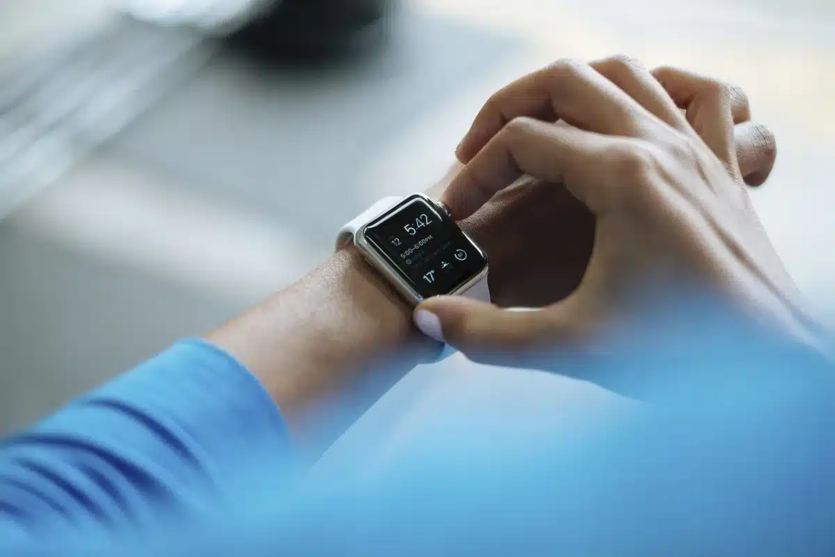 Close-up of an anonymous fitness band beside a smartphone on a retail counter, neutral background, no logos, one hand reaching blurred in background