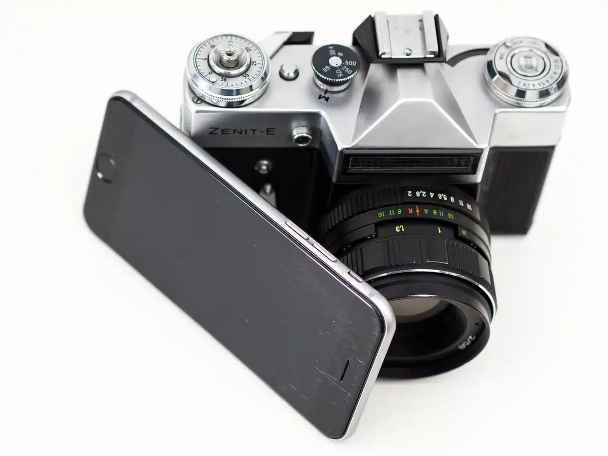 Anonymous hands holding two generic phones side by side comparing screens, one showing a bright video, the other a camera app interface — faces not visible