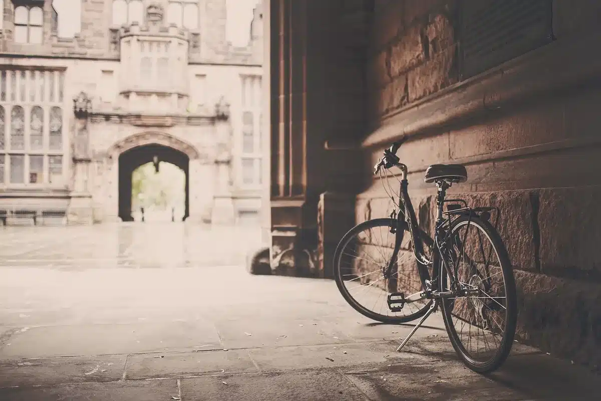 Anonymous cyclist pushing a folded e-bike beside a sidewalk bench, city background blurred