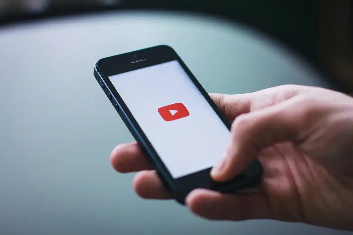 Anonymous hands holding a smartphone showing a generic video player interface on a dark background, dim ambient light, thumb poised over play button