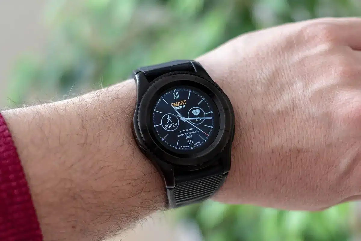 Close-up of an unbranded round smartwatch face on a neutral table, small compact size visible, leather strap beside it