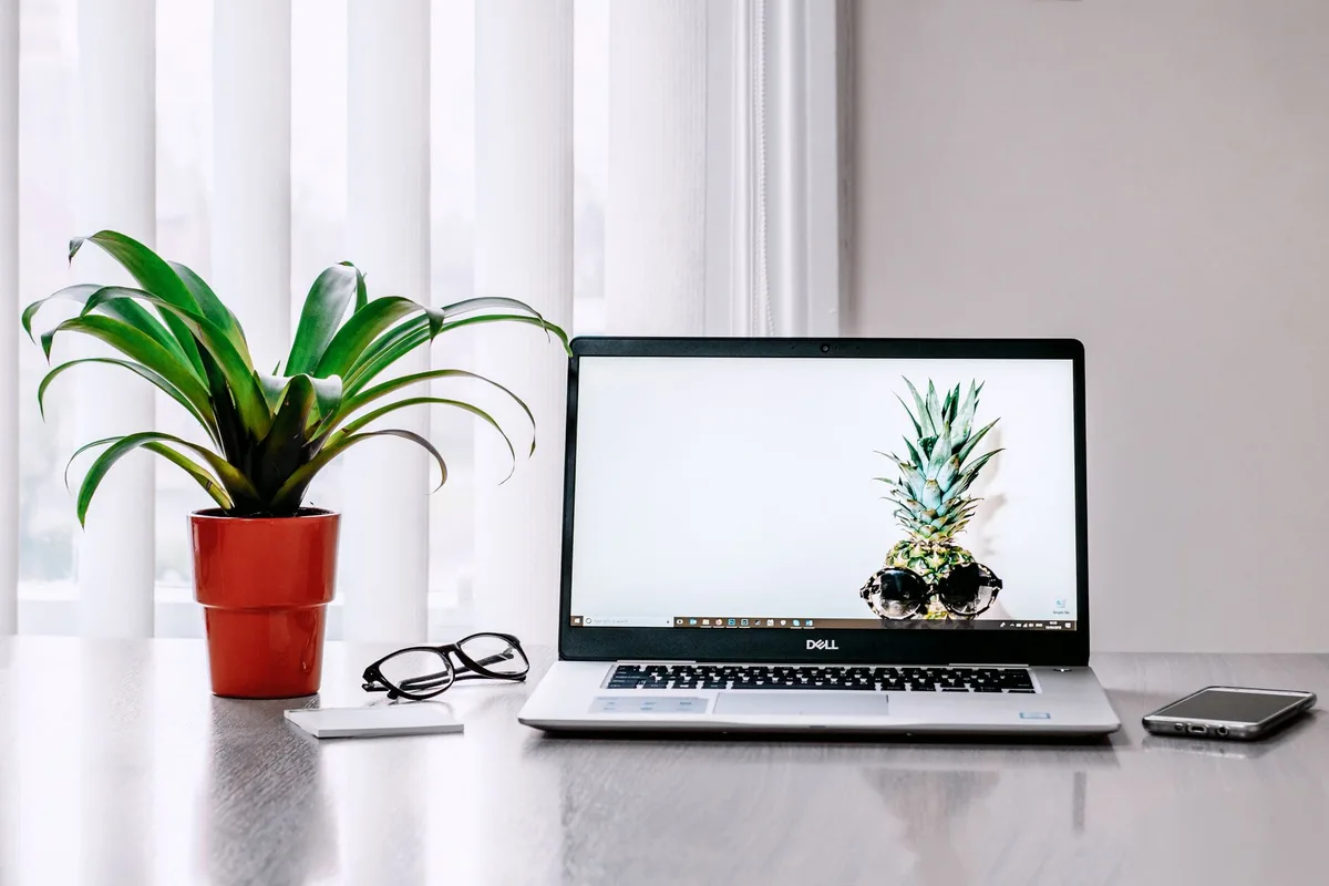 A closed modern laptop on a tidy desk, screen faintly glowing, no logos visible, a notebook and pen beside it