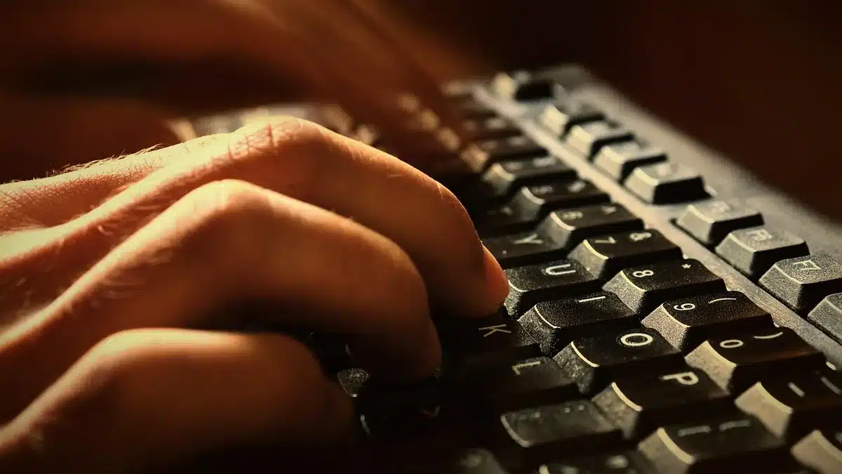 An open laptop showing a dark OLED screen with deep blacks, anonymous hands typing blurred in motion, neutral background, no branding
