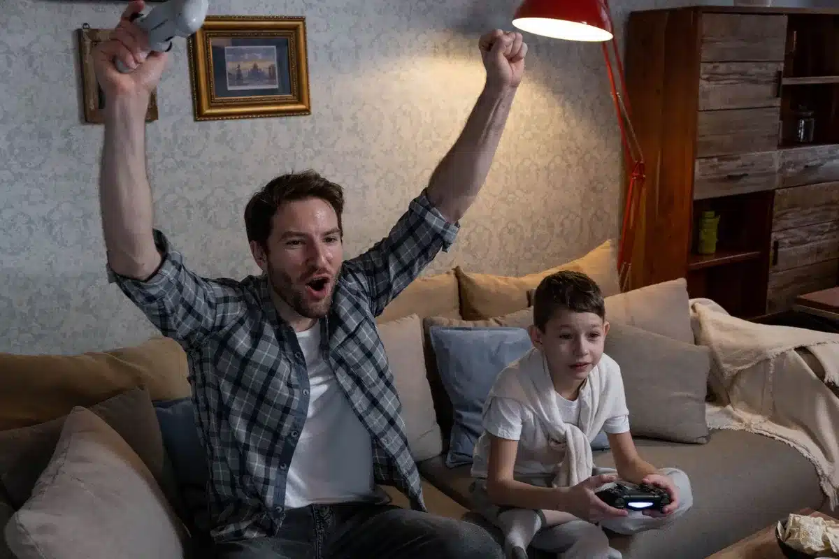 Empty gaming living room with an unbranded console and a TV showing a generic subscription menu, two anonymous silhouettes in the background