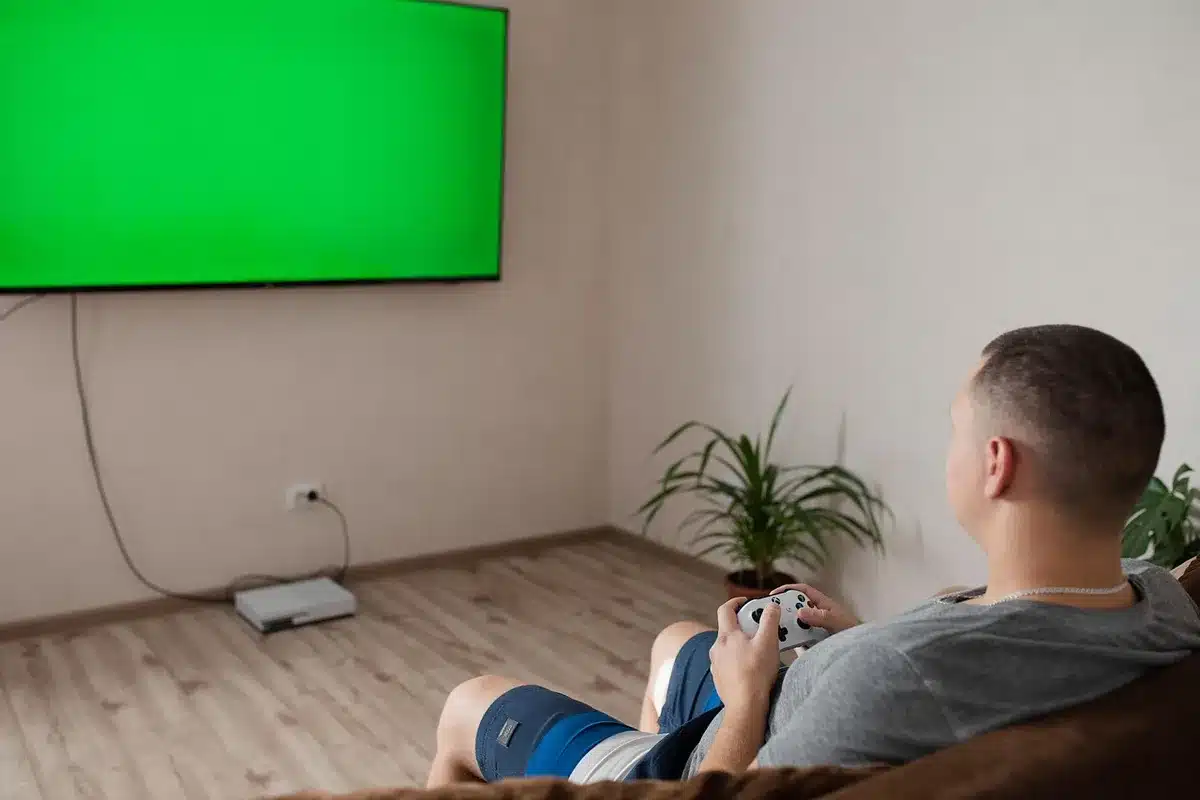 empty modern living room with an unbranded game console on a side table, a TV screen glow, and a closed retail box nearby