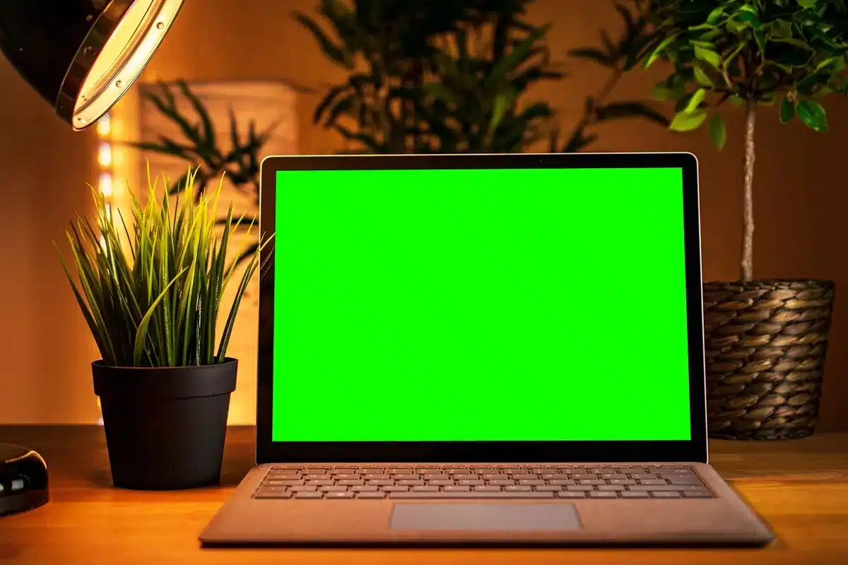 Two anonymous silhouettes leaning over a table lit by a monitor showing performance overlays, one pointing at a chart while the other holds a notebook — collaborative PC troubleshooting scene