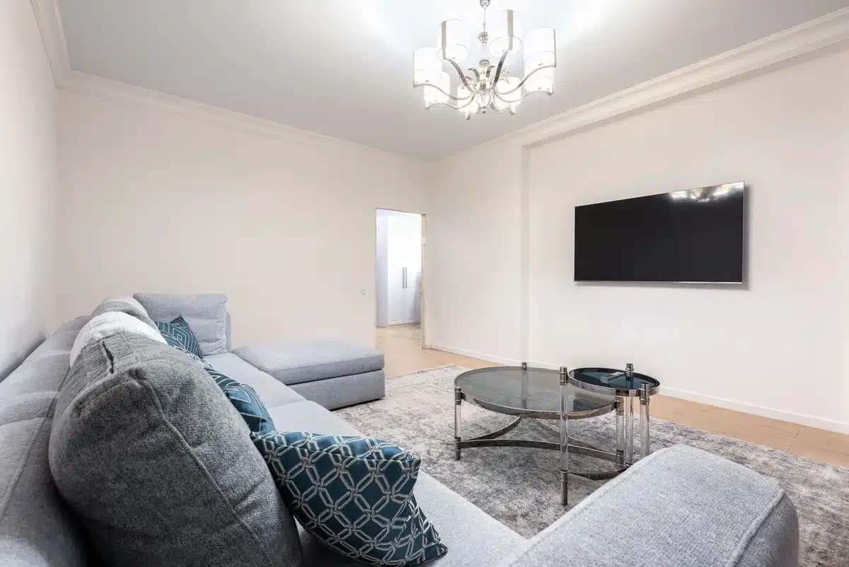 Wide living room with an unbranded 65-inch TV on a slim stand displaying abstract colorful test pattern, minimal decor, no logos or people