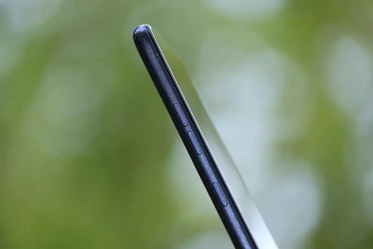 Rear view of a white mid-range smartphone on a table with a visible triple camera module and its retail box beside it