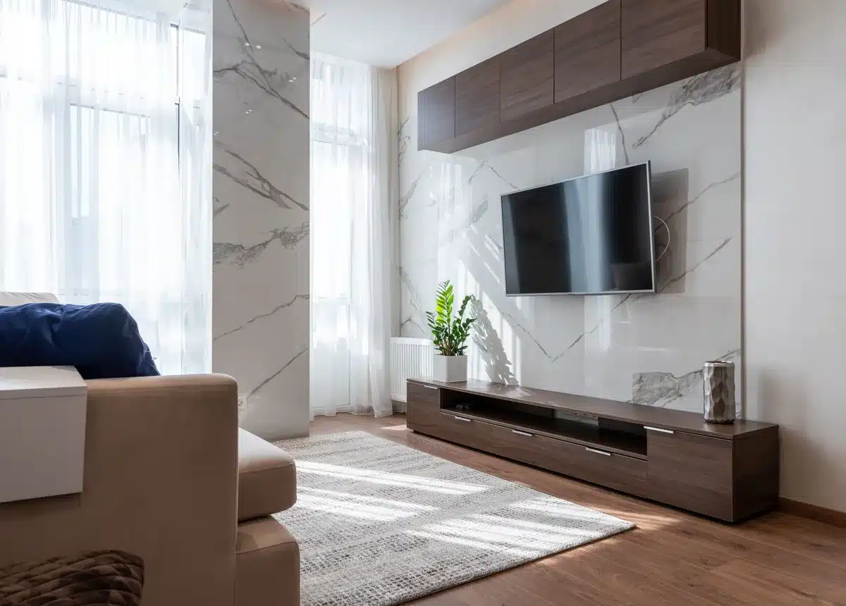 An empty living-room scene with a 55-inch unbranded TV on a low media unit, warm lamp light, and a blurred game controller on a coffee table