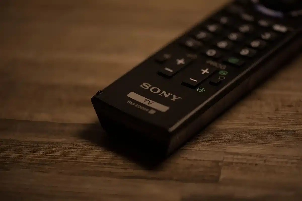 Close view of an anonymous hand holding a remote control with a glowing AI button, blurred unbranded TV in background, evening interior