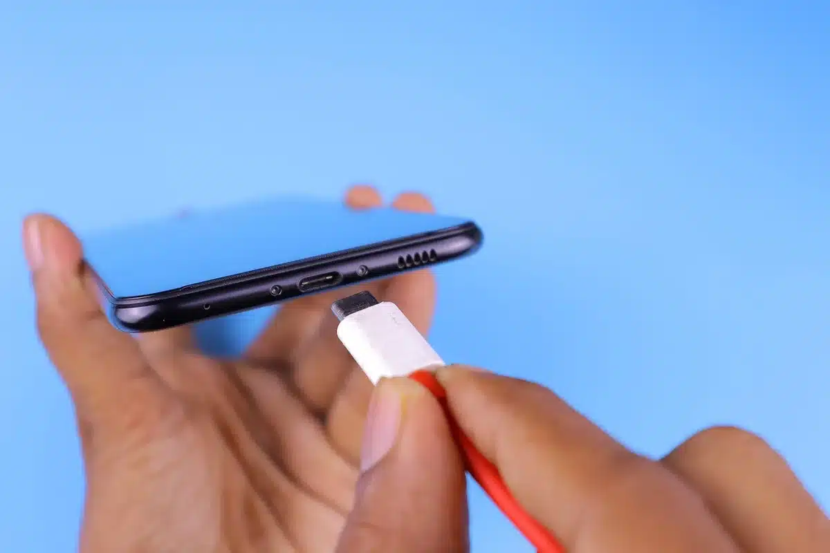 Close-up of an anonymous hand holding an unbranded USB‑C cable near an anonymous power adapter on a plain table, warm indoor lighting, no identifiable marks