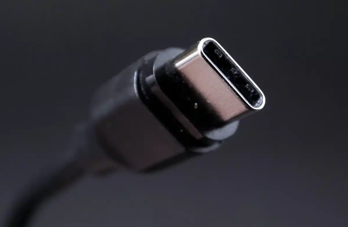 Close-up of an anonymous hand plugging a USB-C cable into a generic phone on a wooden desk, no brand or logo visible