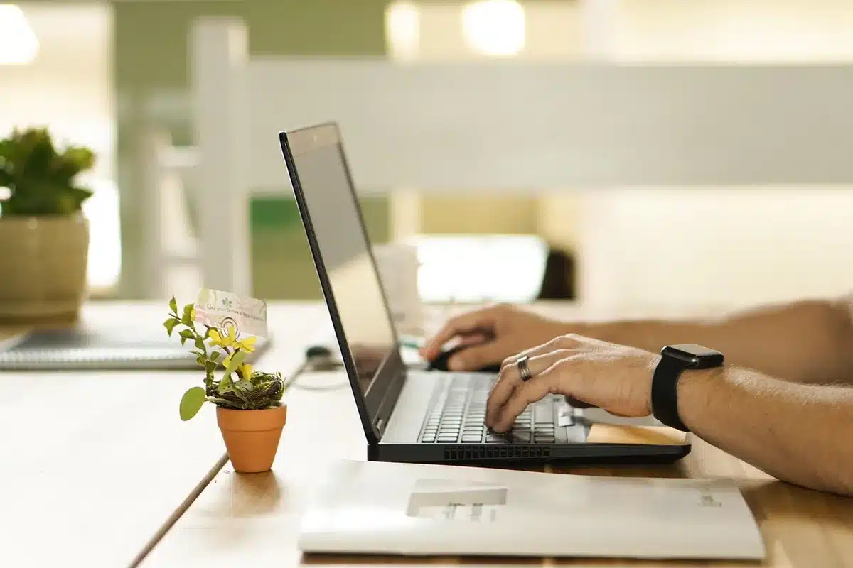 Escritorio de oficina con portátil, tableta y manos sobre el teclado