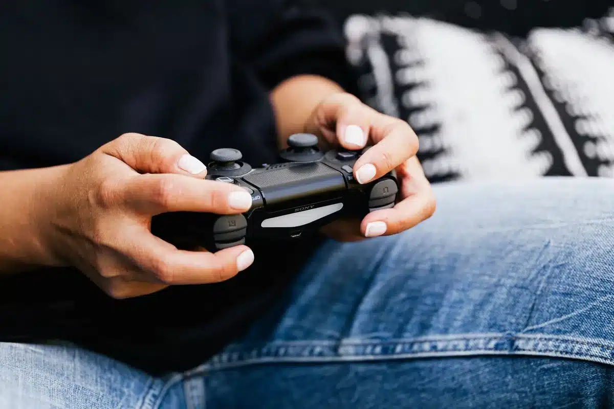 Close-up of an anonymous player holding an unbranded controller in front of a large TV showing a blurred Hyrule landscape, warm living-room setting